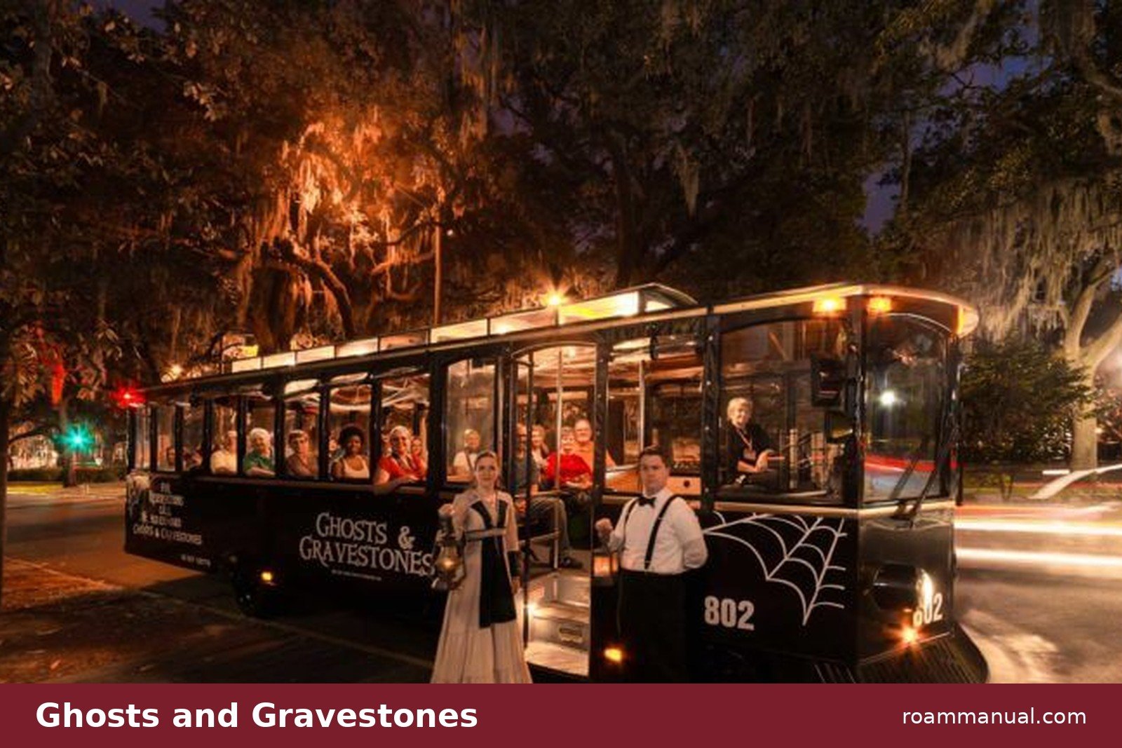 The black Ghosts and Gravestones trolley with costumed hosts on a Savannah street at night, under Spanish moss